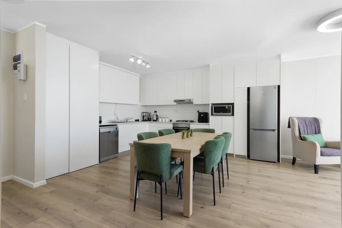 White kitchen and green dining chairs beside the ocean-facing living room