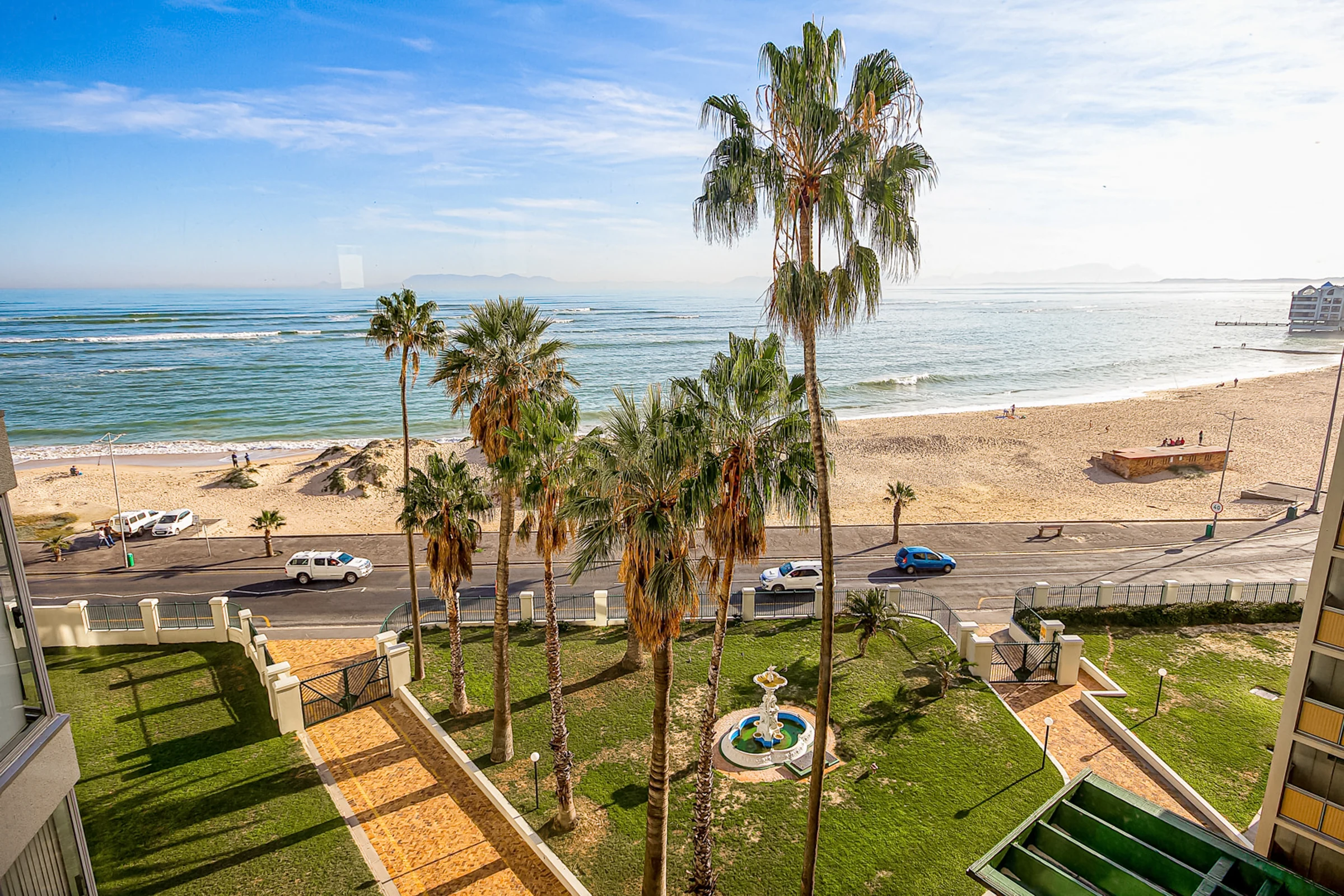 Strand beach and palm-lined promenade in front of ZenDen Destinations
